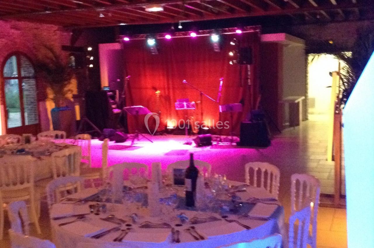 Salle de réception avec tables dressées et une scène éclairée en rose équipée de micros et instruments.