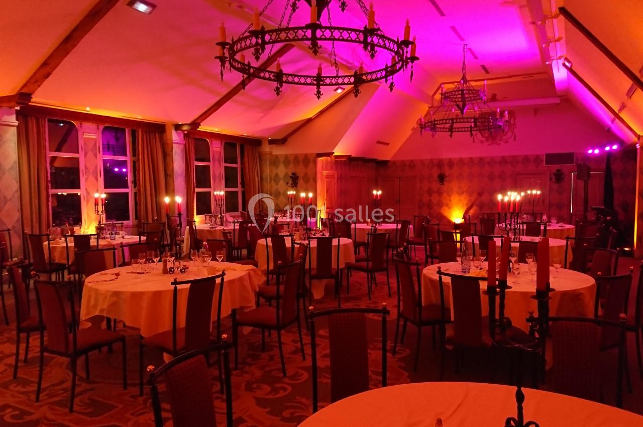 Salle de réception décorée avec des tables rondes, des chandeliers allumés et un éclairage tamisé aux tons chauds.