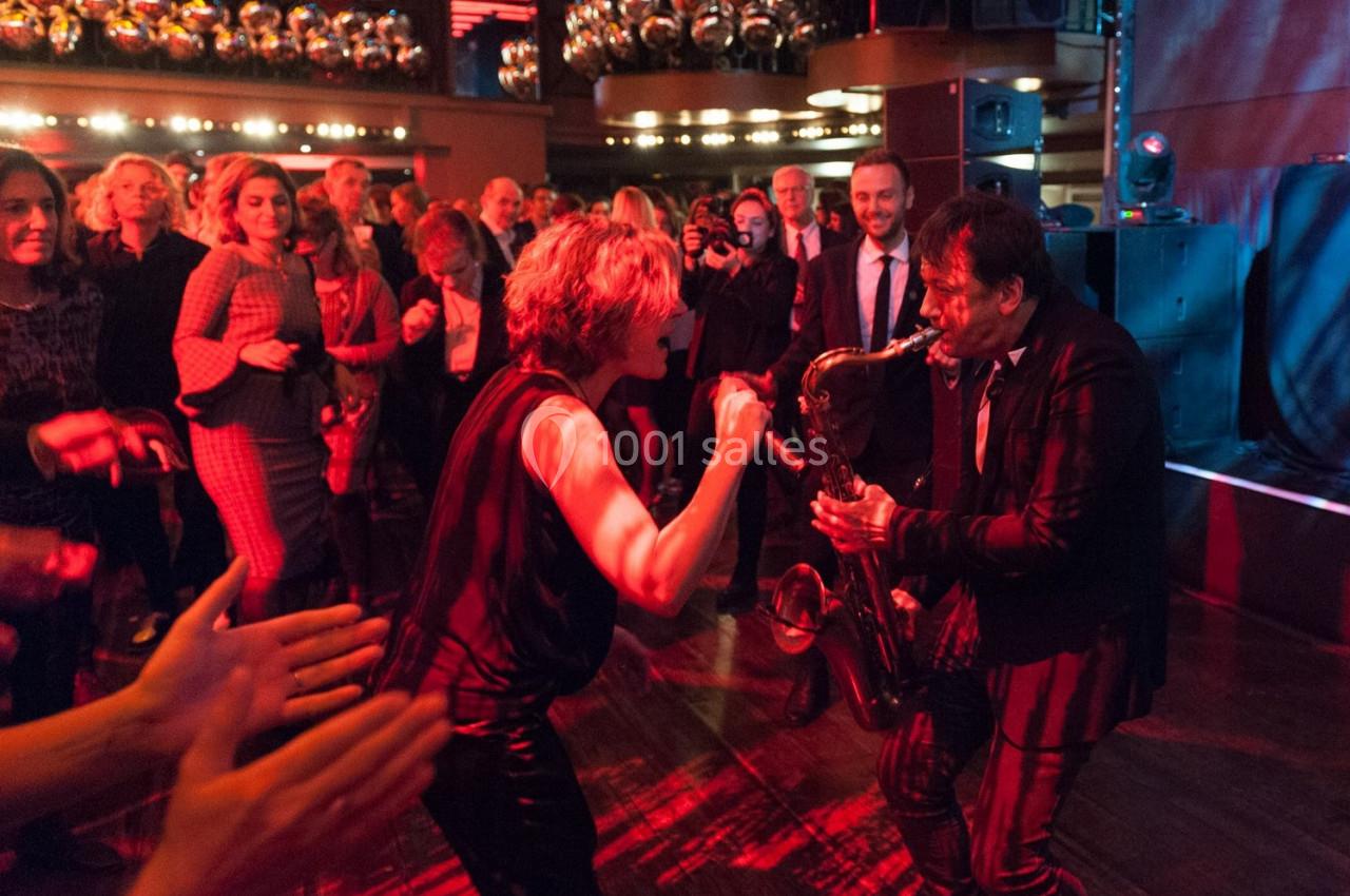 Un musicien joue du saxophone au milieu d'une foule dansante dans une ambiance festive et éclairage tamisé.