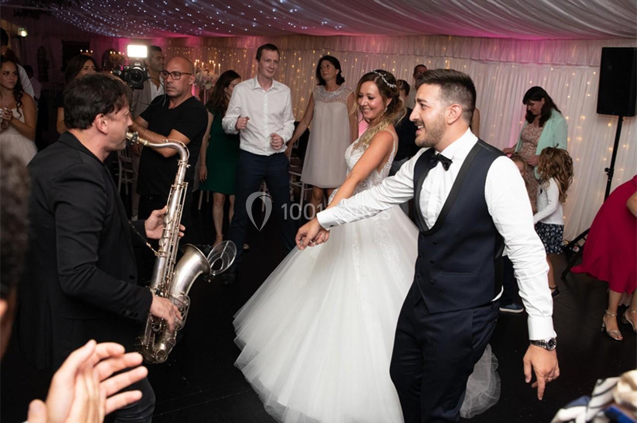 Un saxophoniste joue lors d'une réception de mariage, entouré d'invités dansant sous un plafond illuminé.