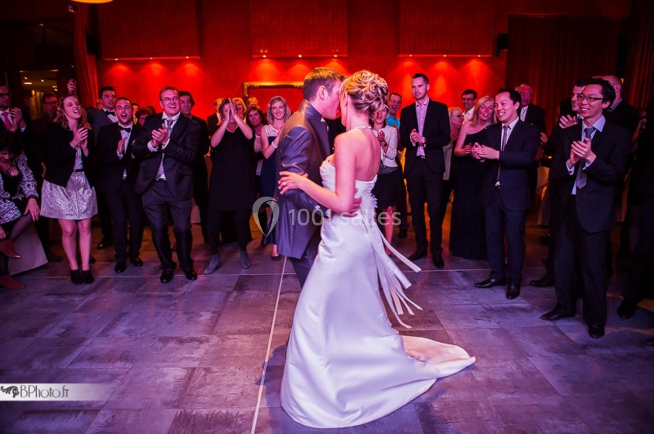 Un couple danse au centre d'une salle, entouré d'invités applaudissant dans une ambiance festive et éclairage chaleureux.