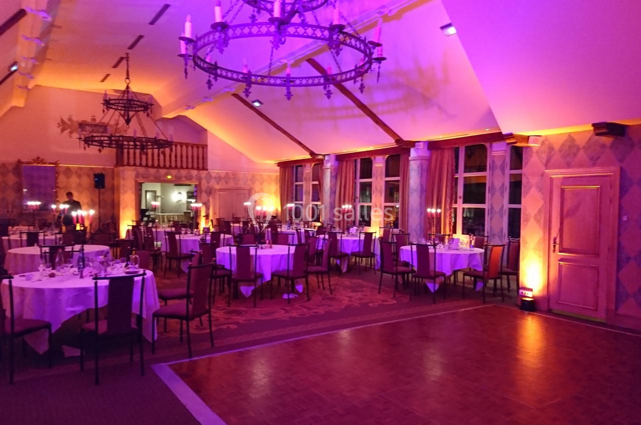 Salle de réception décorée avec des tables rondes dressées, éclairage tamisé et lustre suspendu.