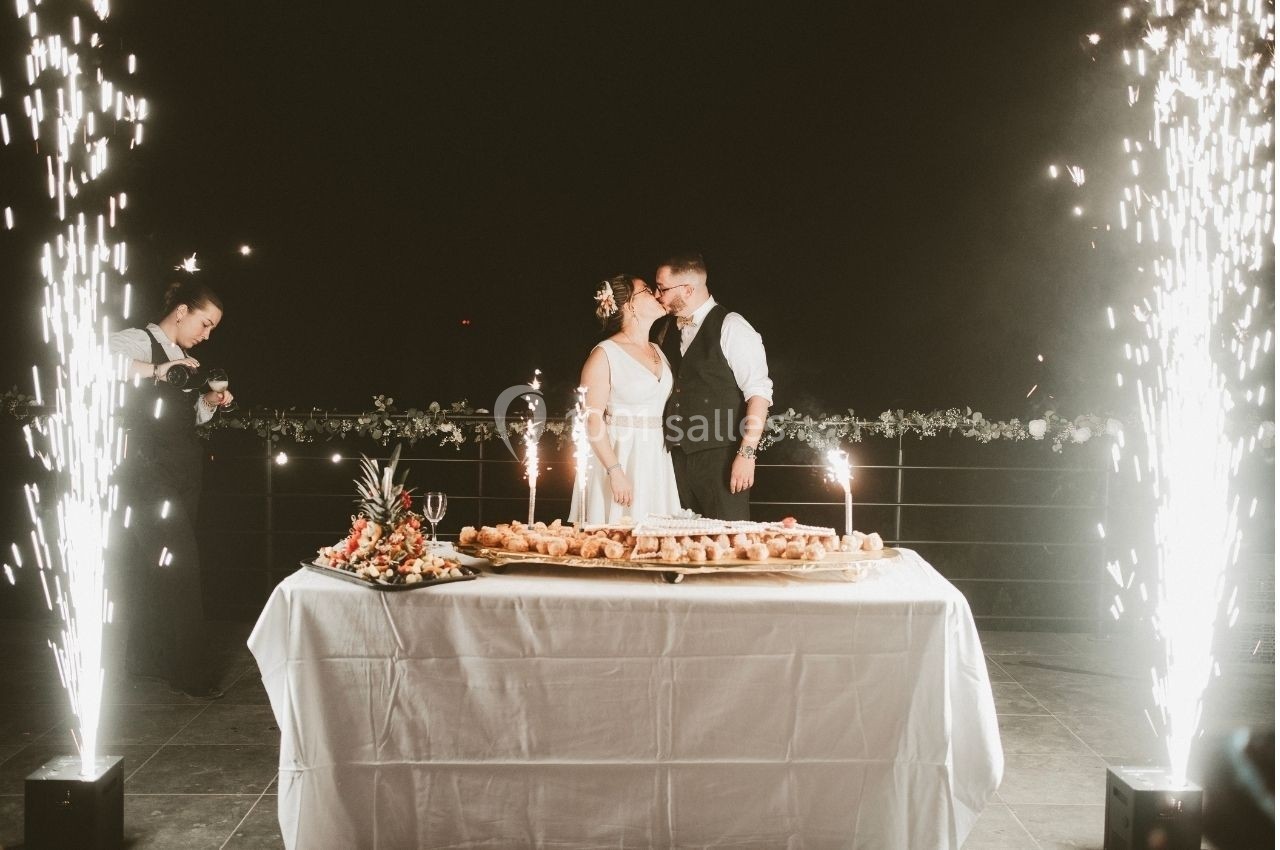Location salle Saint-Genès-de-Lombaud (Gironde) - Domaine du Château Icla #7 Un couple de mariés se tient près d'une table garnie de desserts, entouré de fontaines lumineuses.