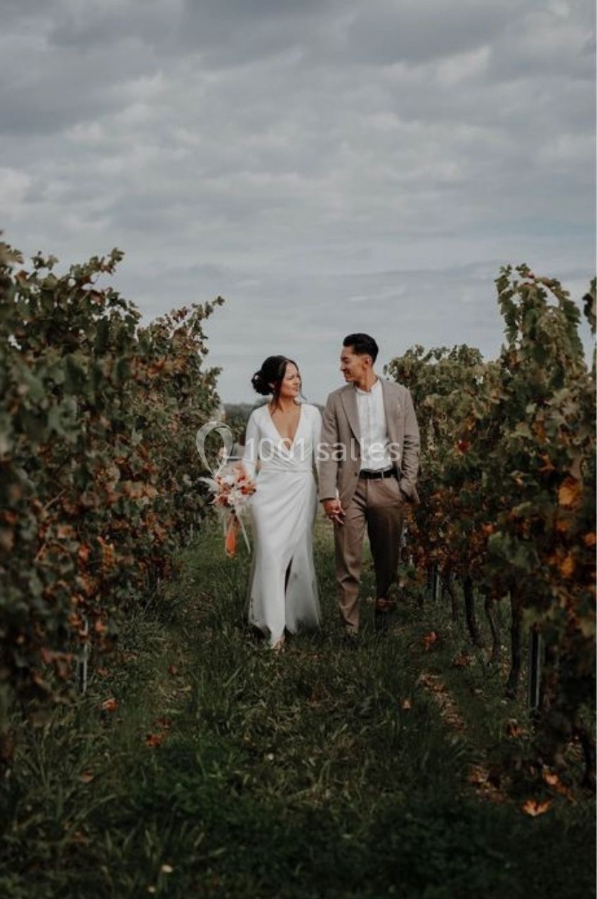 Location salle Saint-Genès-de-Lombaud (Gironde) - Domaine du Château Icla #4 Un couple marche main dans la main dans un vignoble sous un ciel nuageux.