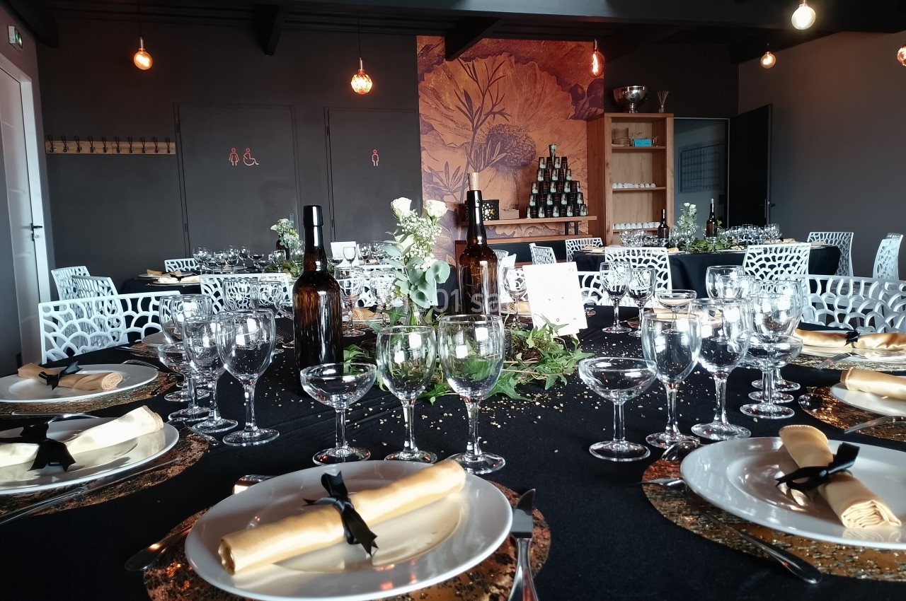 Location salle Saint-Genès-de-Lombaud (Gironde) - Domaine du Château Icla #10 Table élégamment dressée avec nappes noires, vaisselle raffinée, décor floral et bouteilles de vin dans une salle sombre.