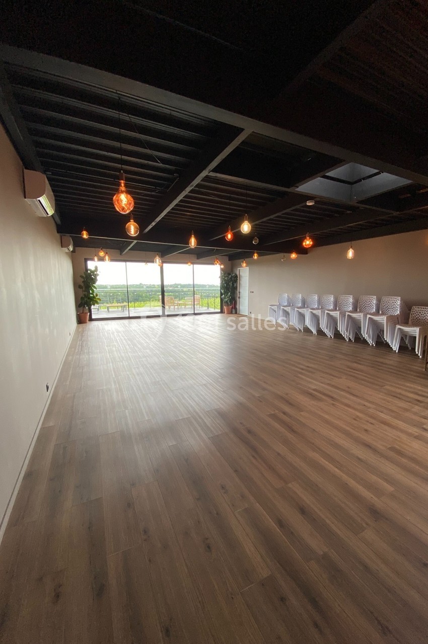 Location salle Saint-Genès-de-Lombaud (Gironde) - Domaine du Château Icla #12 Salle spacieuse avec parquet, chaises alignées à droite, grandes baies vitrées donnant sur un extérieur verdoyant.