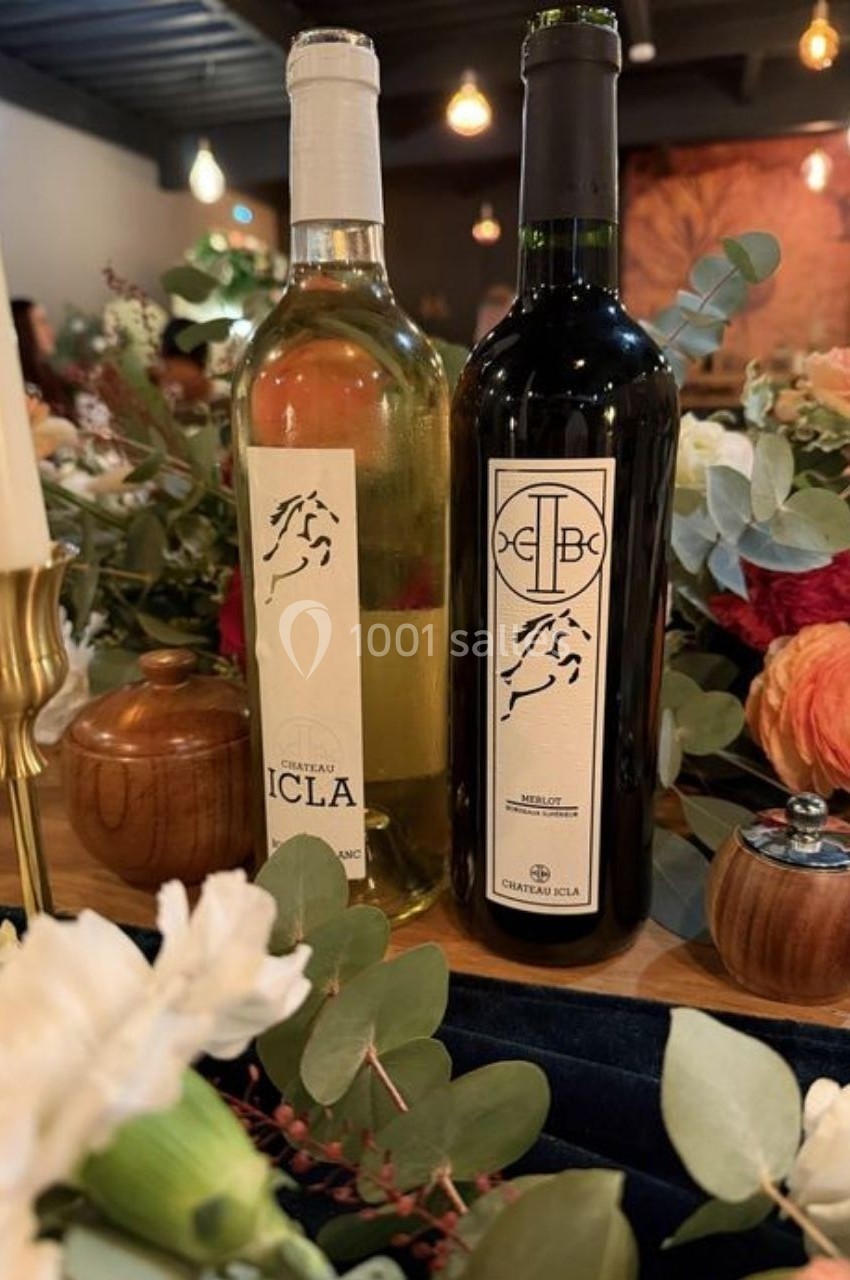 Location salle Saint-Genès-de-Lombaud (Gironde) - Domaine du Château Icla #13 Deux bouteilles de vin, blanc et rouge, posées sur une table décorée de fleurs et de feuillage.