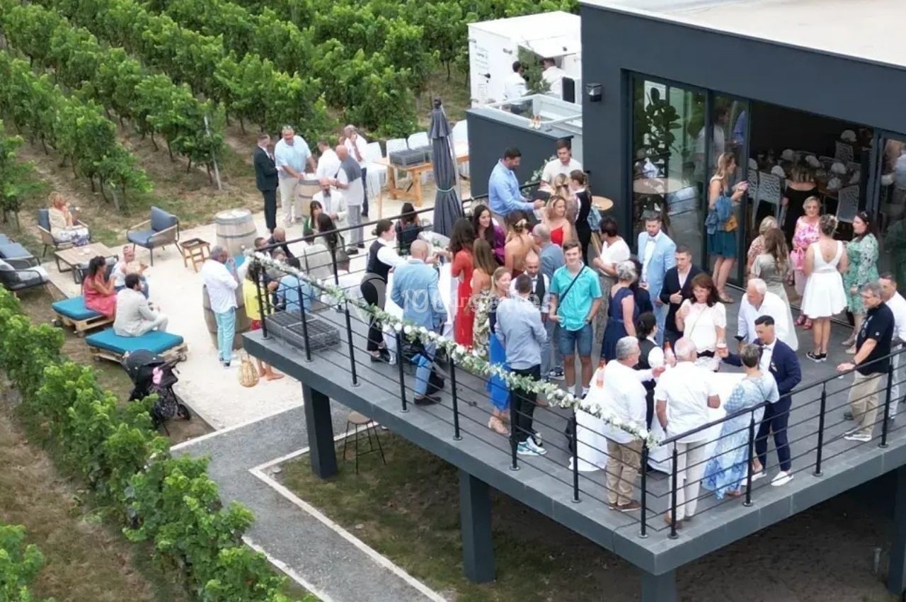 Location salle Saint-Genès-de-Lombaud (Gironde) - Domaine du Château Icla #18 Groupe de personnes réunies sur une terrasse moderne surplombant un vignoble, lors d'un événement en plein air.