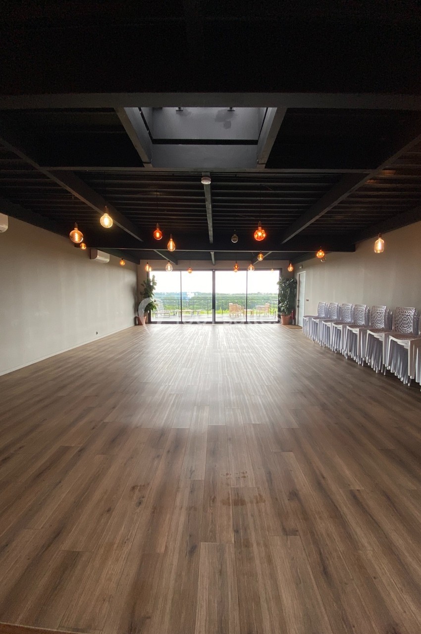 Location salle Saint-Genès-de-Lombaud (Gironde) - Domaine du Château Icla #27 Salle vide avec parquet en bois, éclairée par des suspensions lumineuses, donnant sur une baie vitrée avec vue extérieure.