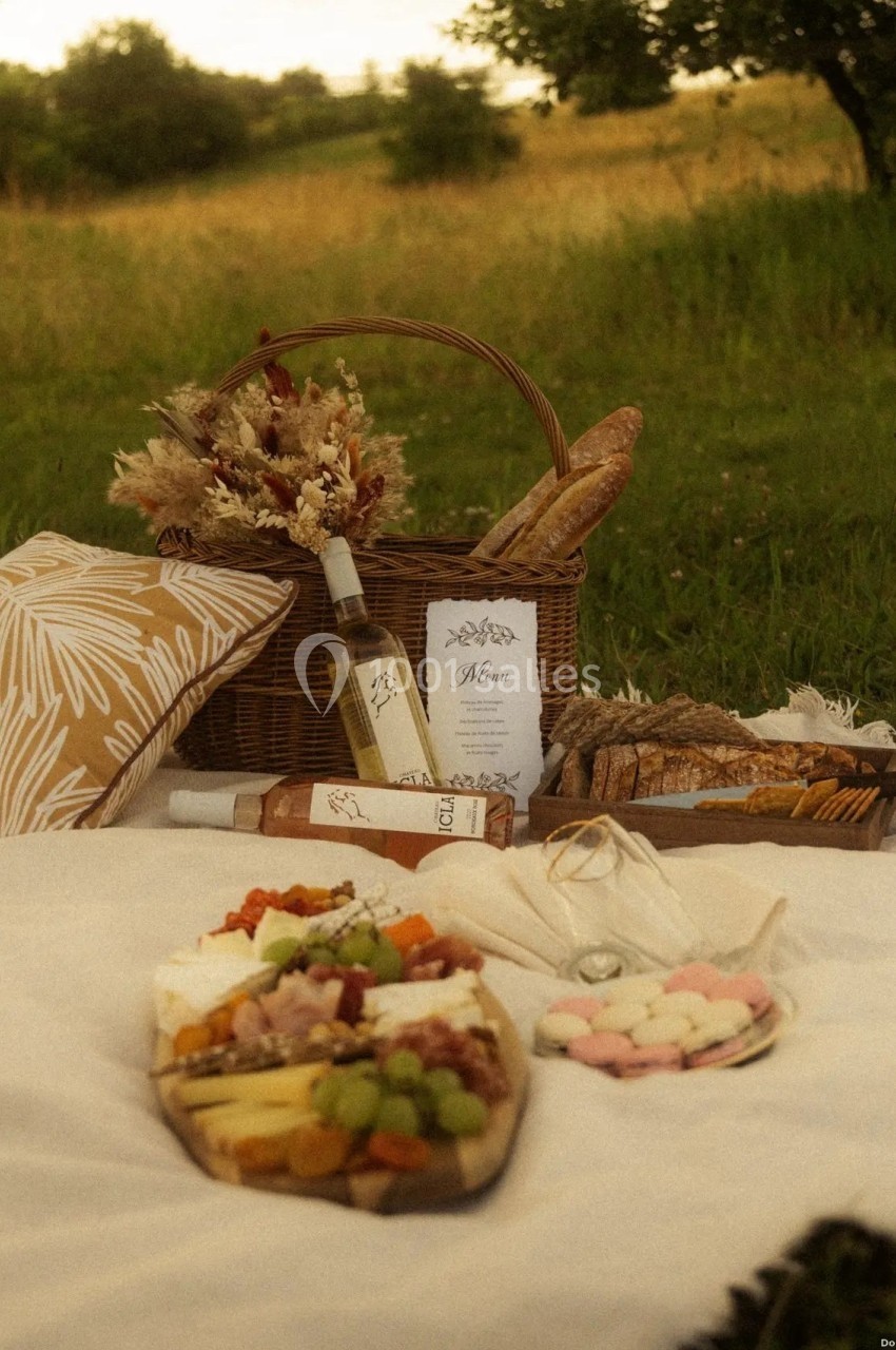 Location salle Saint-Genès-de-Lombaud (Gironde) - Domaine du Château Icla #35 Pique-nique champêtre avec panier en osier, pain, fruits, fromage, macarons et bouteille de vin sur une nappe blanche.
