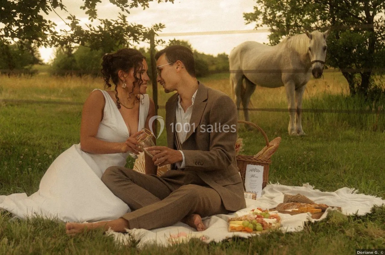 Location salle Saint-Genès-de-Lombaud (Gironde) - Domaine du Château Icla #39 Un couple assis sur une couverture lors d'un pique-nique champêtre, avec un cheval en arrière-plan.