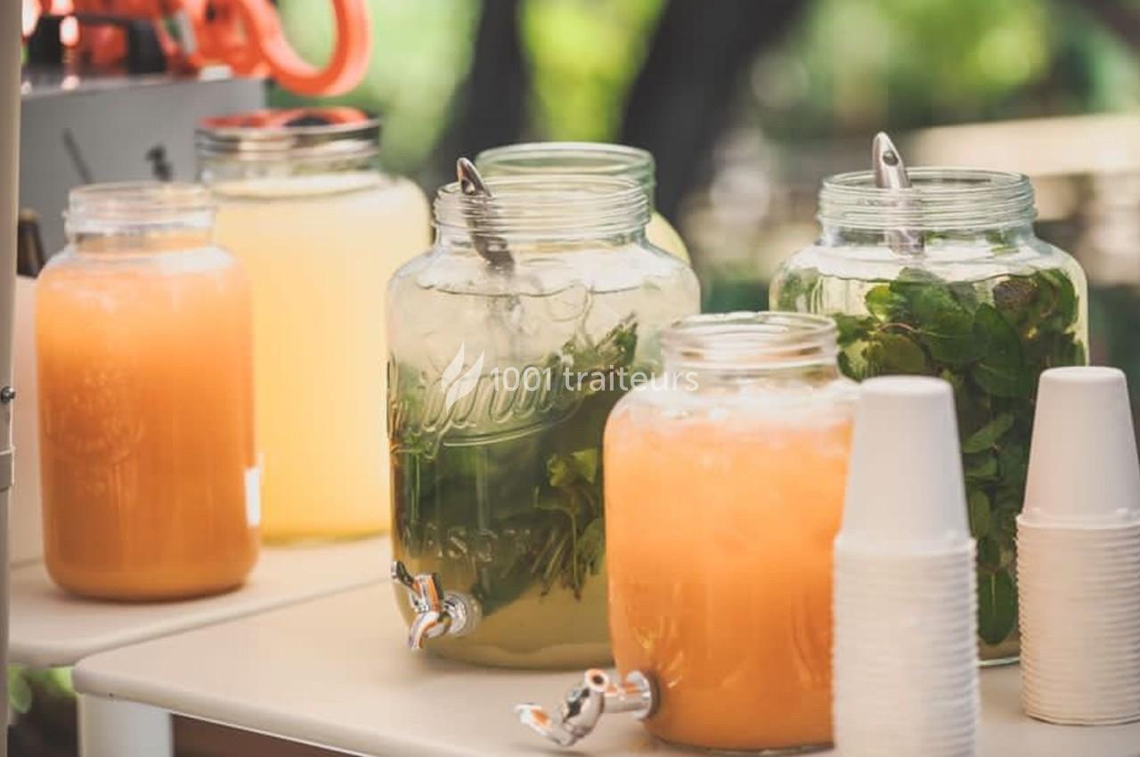 Bocaux de boissons fraîches, dont une à base de menthe, disposés sur une table avec des gobelets en plastique.