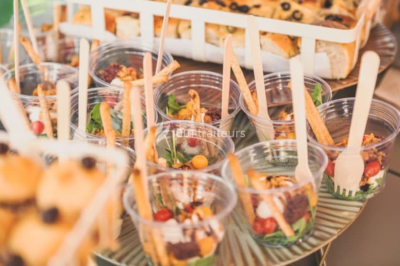 Des verrines garnies de légumes frais, gressins et noix, disposées sur une table avec des pains en arrière-plan.