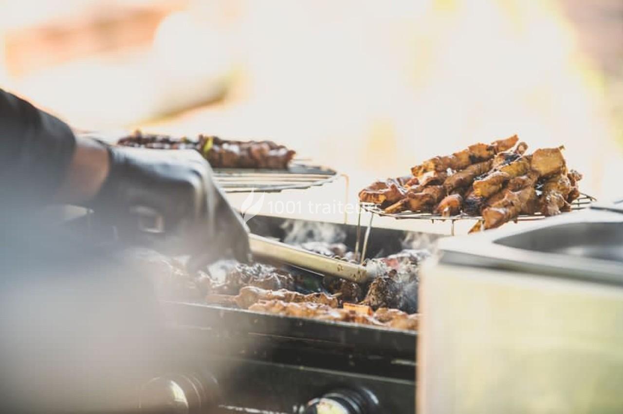 Personne en gant noir retournant des brochettes de viande grillées sur un barbecue en plein air.