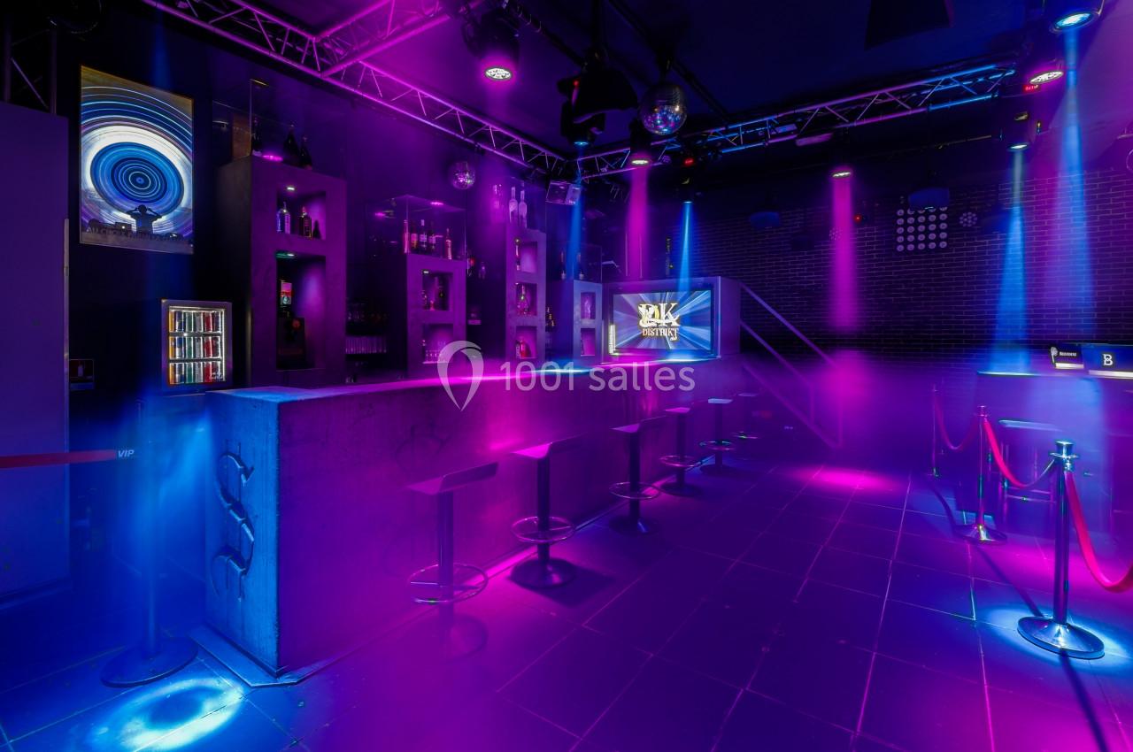 Bar moderne avec éclairage néon violet et bleu, tabourets alignés au comptoir et ambiance de club nocturne.