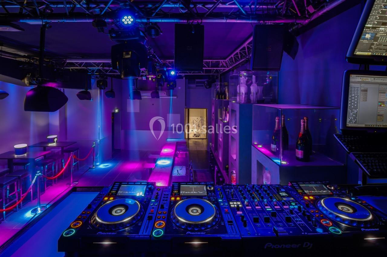 Vue d'une cabine de DJ équipée de platines et d'un éclairage coloré dans une salle de club vide.