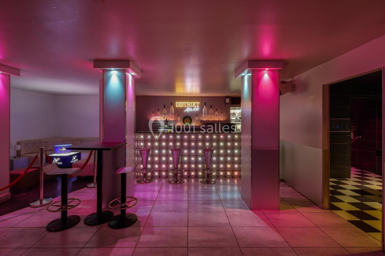 Bar lumineux avec tabourets, éclairage coloré rose et bleu, et comptoir rétroéclairé dans un espace moderne.