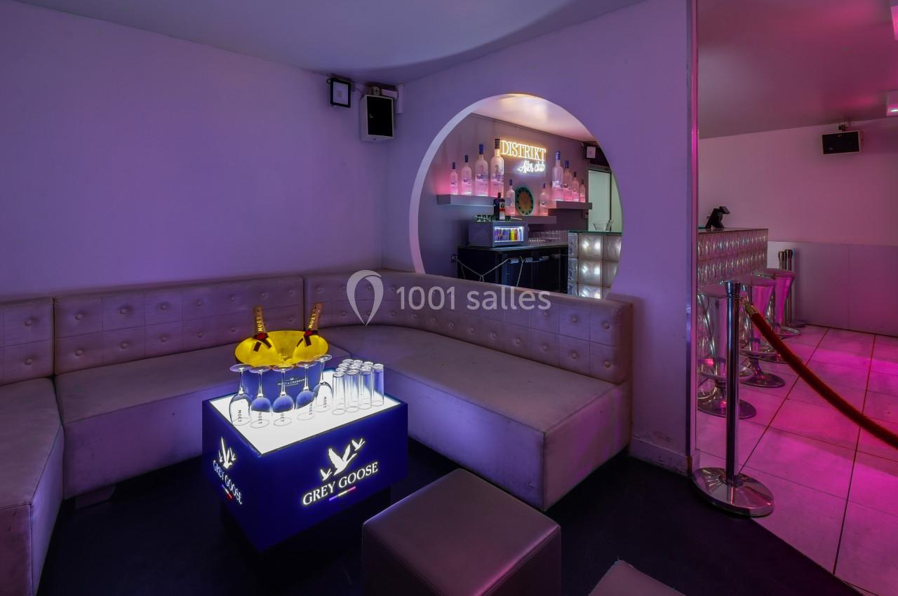 Banquette en cuir beige dans un lounge avec table lumineuse, seau à champagne et bar en arrière-plan.