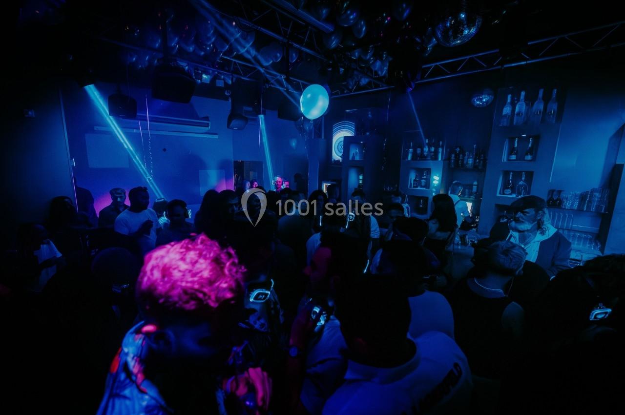 Groupe de personnes dans une discothèque sombre avec éclairages bleus et ambiance festive.