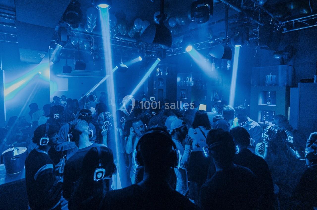 Des personnes dans une discothèque participent à une soirée silencieuse avec des casques audio, éclairées par des lumières…