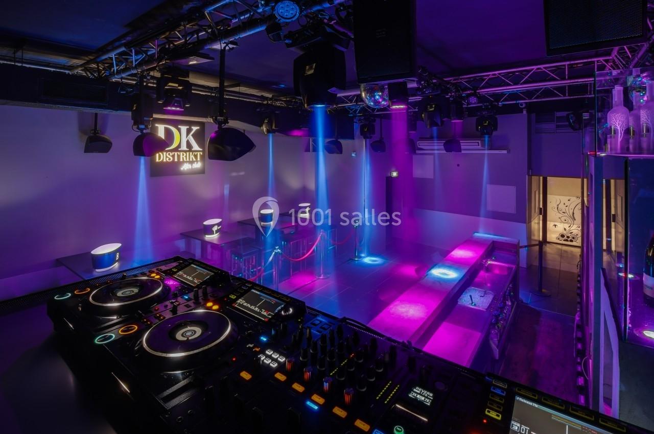 Salle de discothèque avec piste de danse éclairée par des lumières colorées, vue depuis une table de mixage.