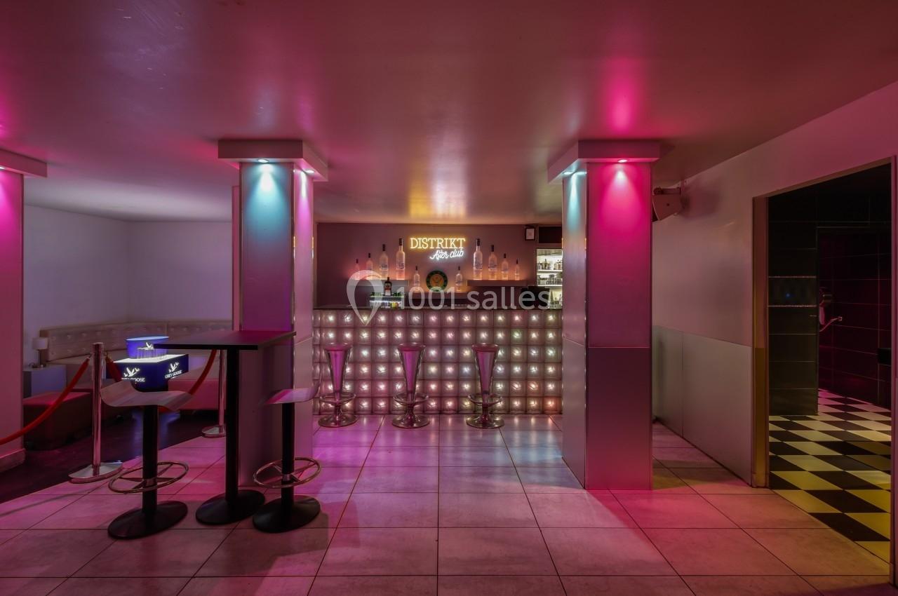 Bar lumineux avec tabourets hauts, éclairage rose et bleu, et comptoir rétroéclairé dans un espace moderne.