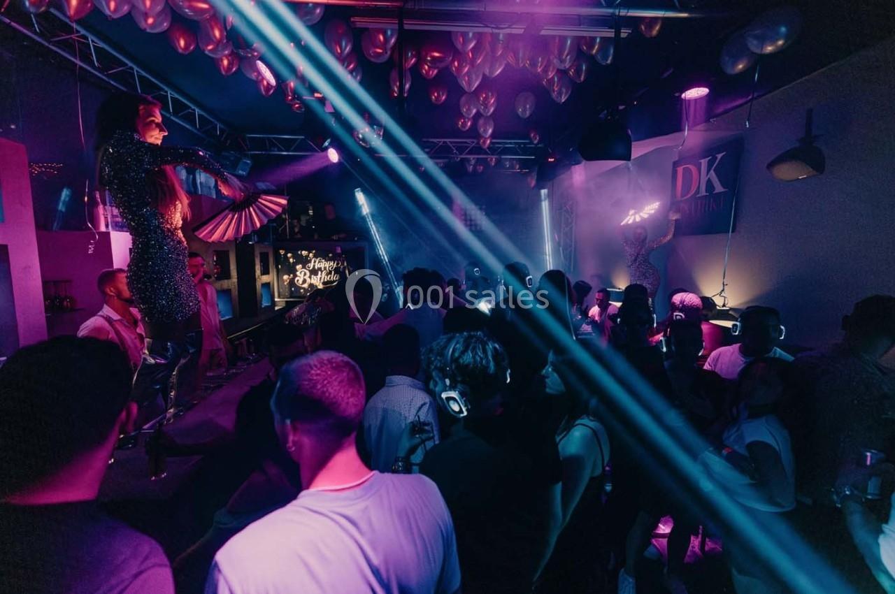 Personnes dansant dans une ambiance festive avec éclairages colorés et artistes sur scène dans un club.