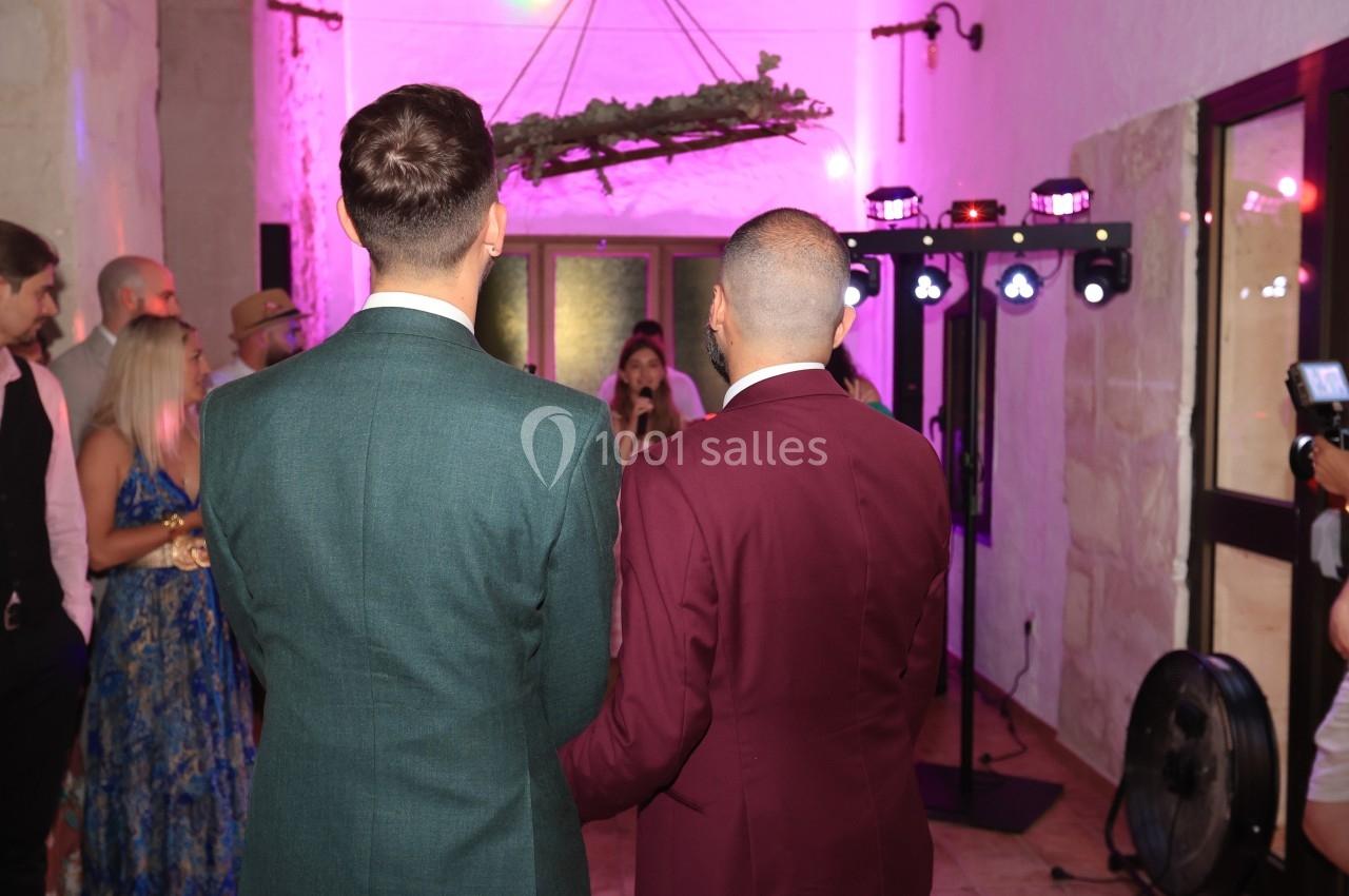 Deux hommes en costumes élégants, vus de dos, assistent à un événement dans une salle éclairée par des lumières roses.