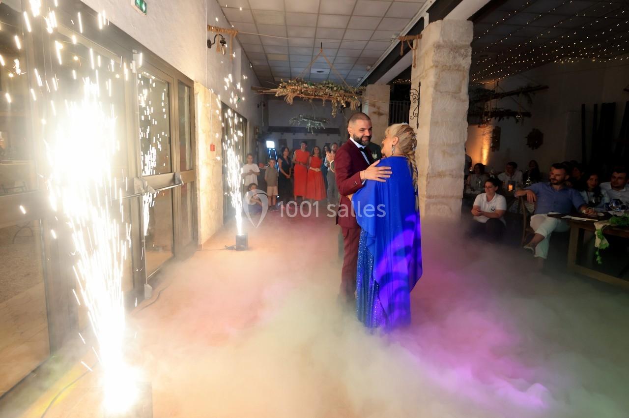 Un couple danse au milieu de fumée colorée et d'étincelles dans une salle décorée, entouré d'invités.