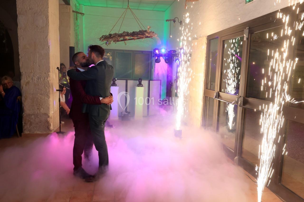 Deux hommes dansent enlacés au milieu de fumée et d'effets lumineux dans une salle de réception.