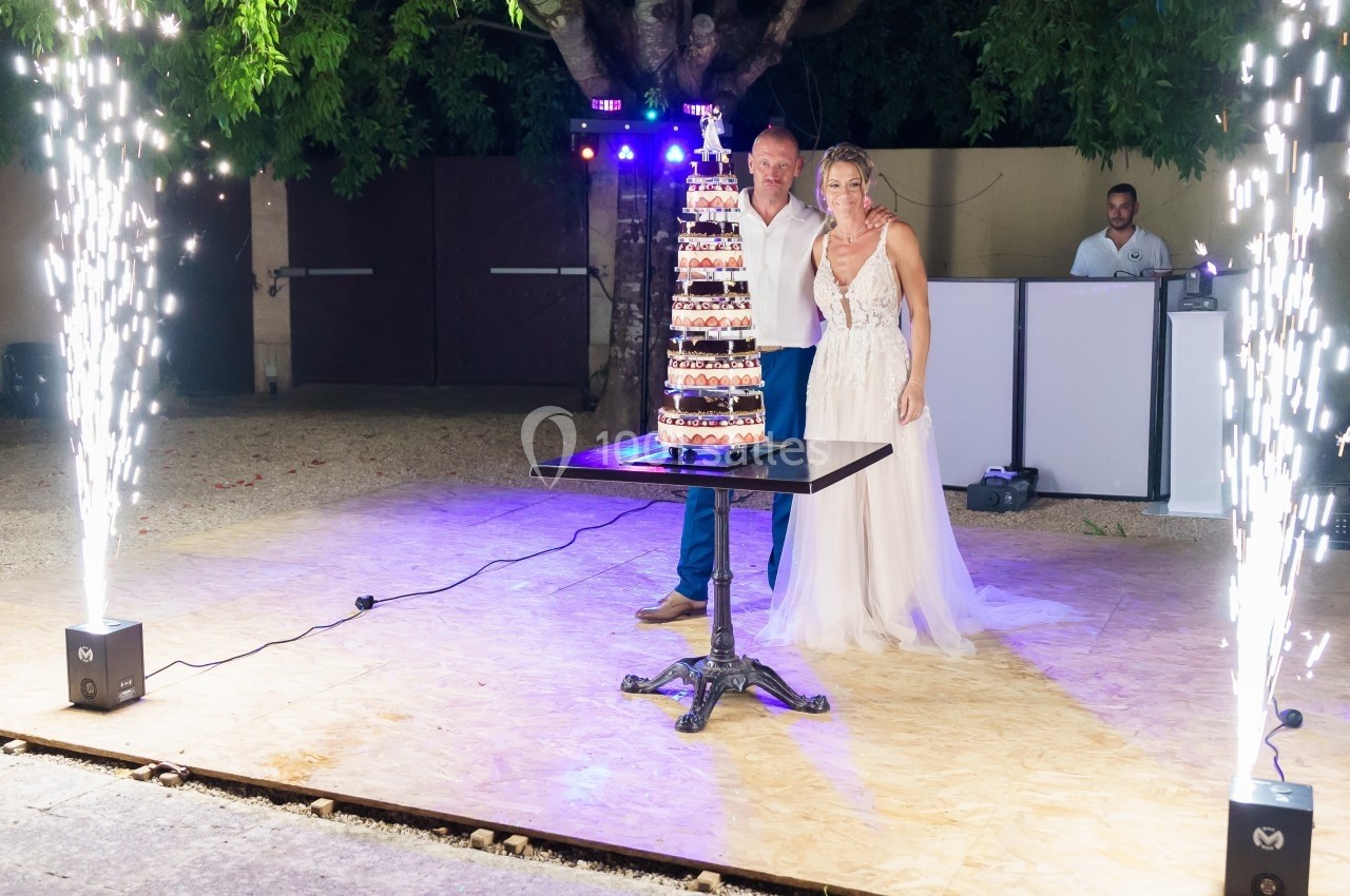 Un couple pose devant une pièce montée éclairée par des étincelles lors d'une célébration en extérieur.
