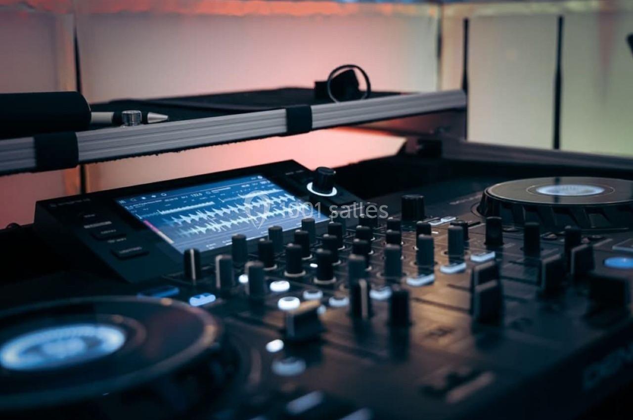 Table de mixage avec platines, boutons et écran affichant une interface audio, éclairée par une lumière tamisée.