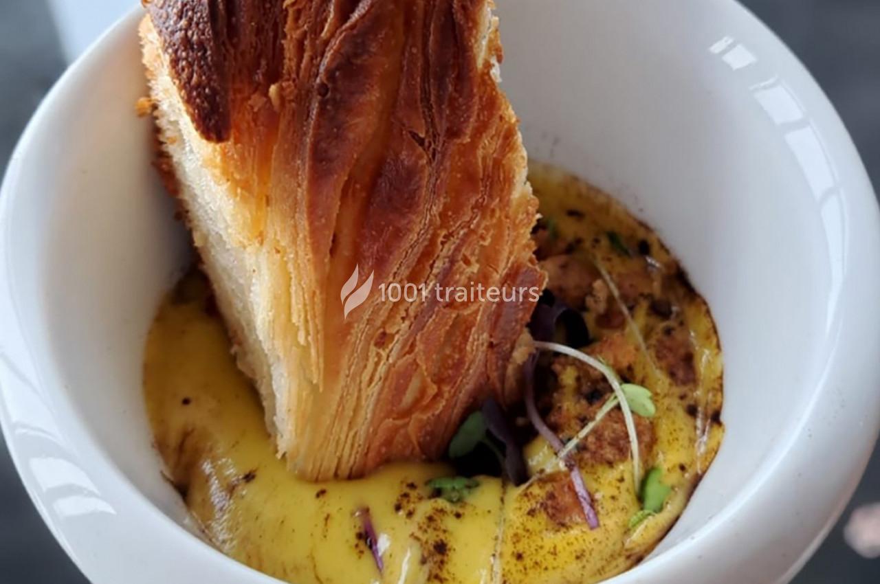 Feuilleté doré plongé dans une sauce crémeuse garnie de jeunes pousses dans un bol blanc.