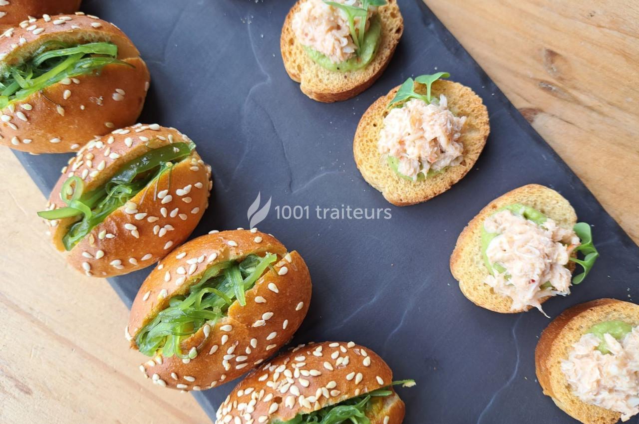 Assortiment de mini-burgers au sésame garnis d'algues et de toasts au crabe sur une ardoise noire.