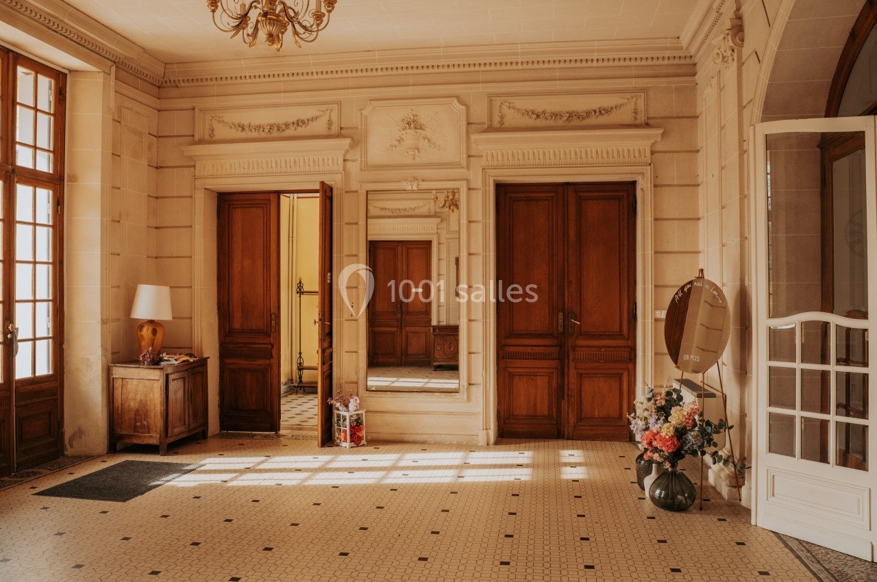 Hall d'entrée lumineux avec carrelage ancien, portes en bois, miroir mural et décoration florale.