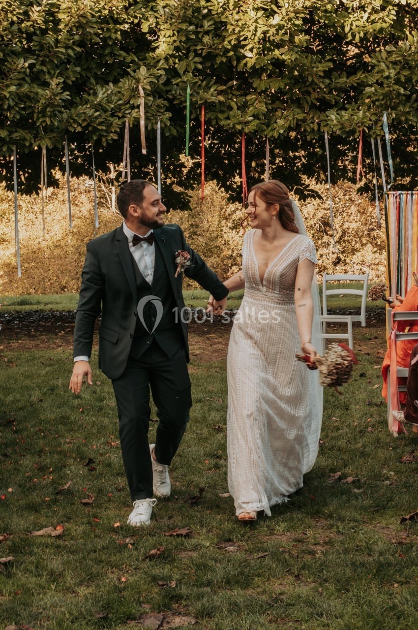 Un couple habillé en tenue de mariage marche sur une pelouse, entouré de décorations colorées en extérieur.