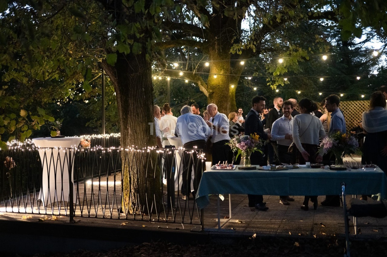 Groupe de personnes discutant sous des guirlandes lumineuses dans un jardin en soirée.