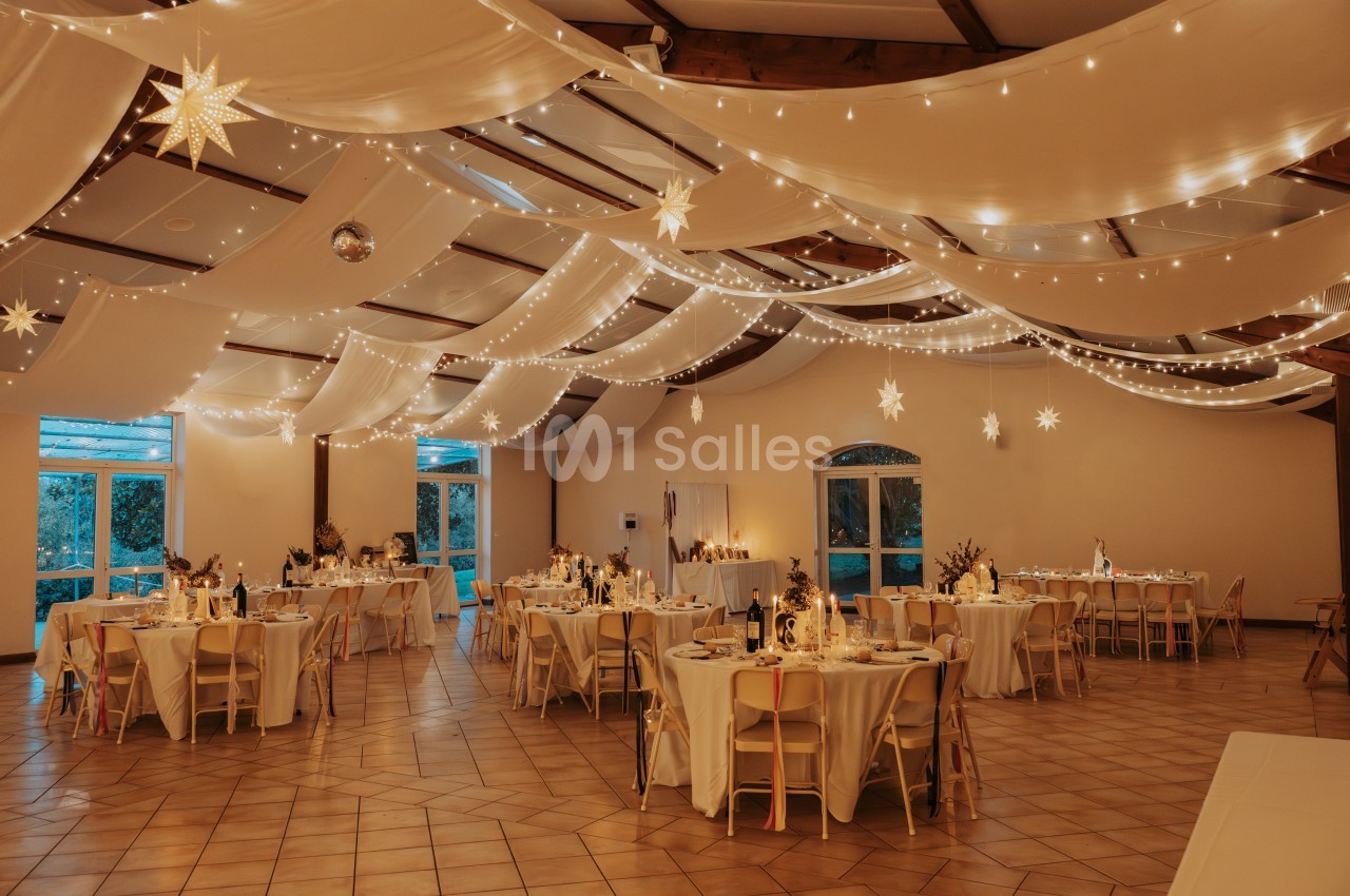 Salle de réception décorée avec des guirlandes lumineuses, des étoiles suspendues et des tables dressées pour un événement.