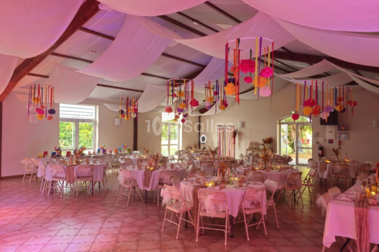 Salle de réception décorée avec des tables dressées, des suspensions colorées et un éclairage chaleureux.