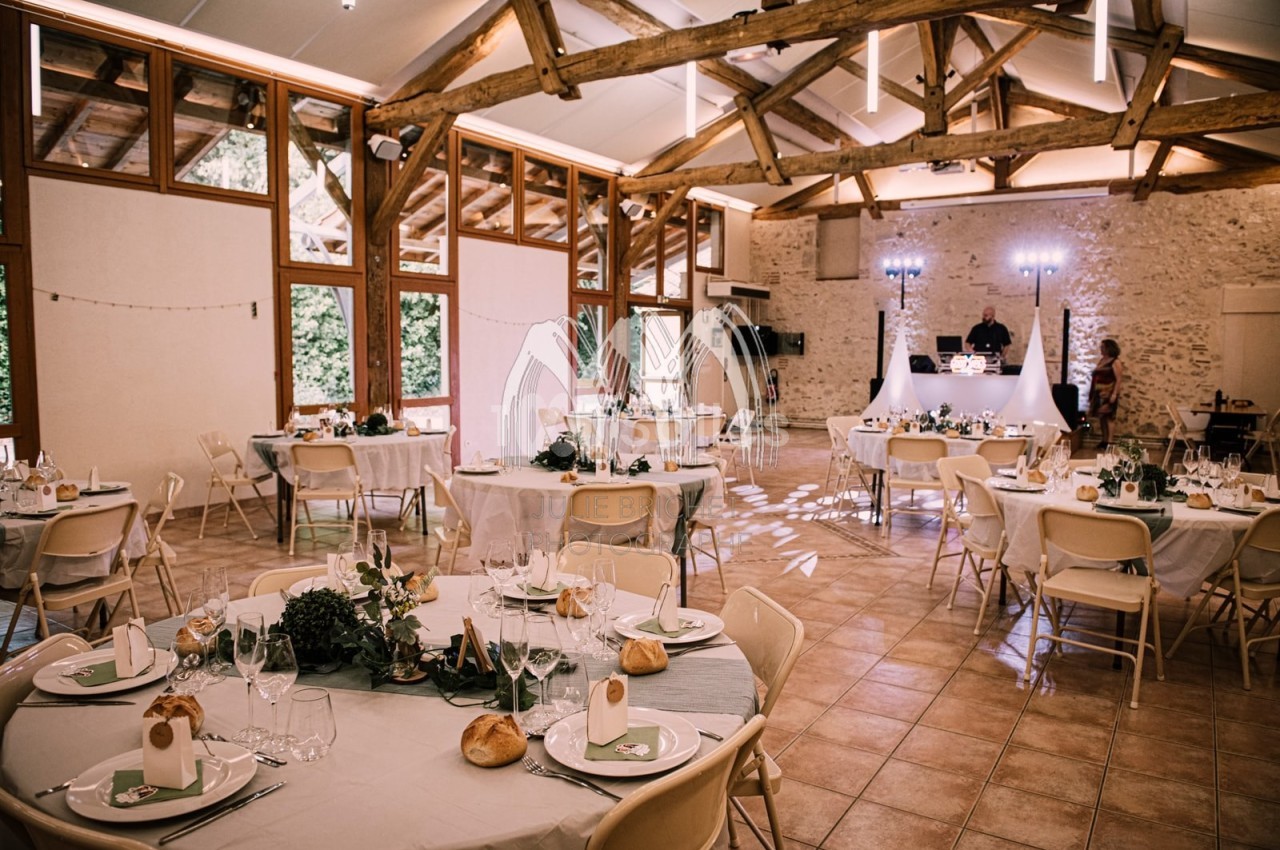 Salle de réception décorée pour un mariage, avec tables rondes dressées et éclairage tamisé.