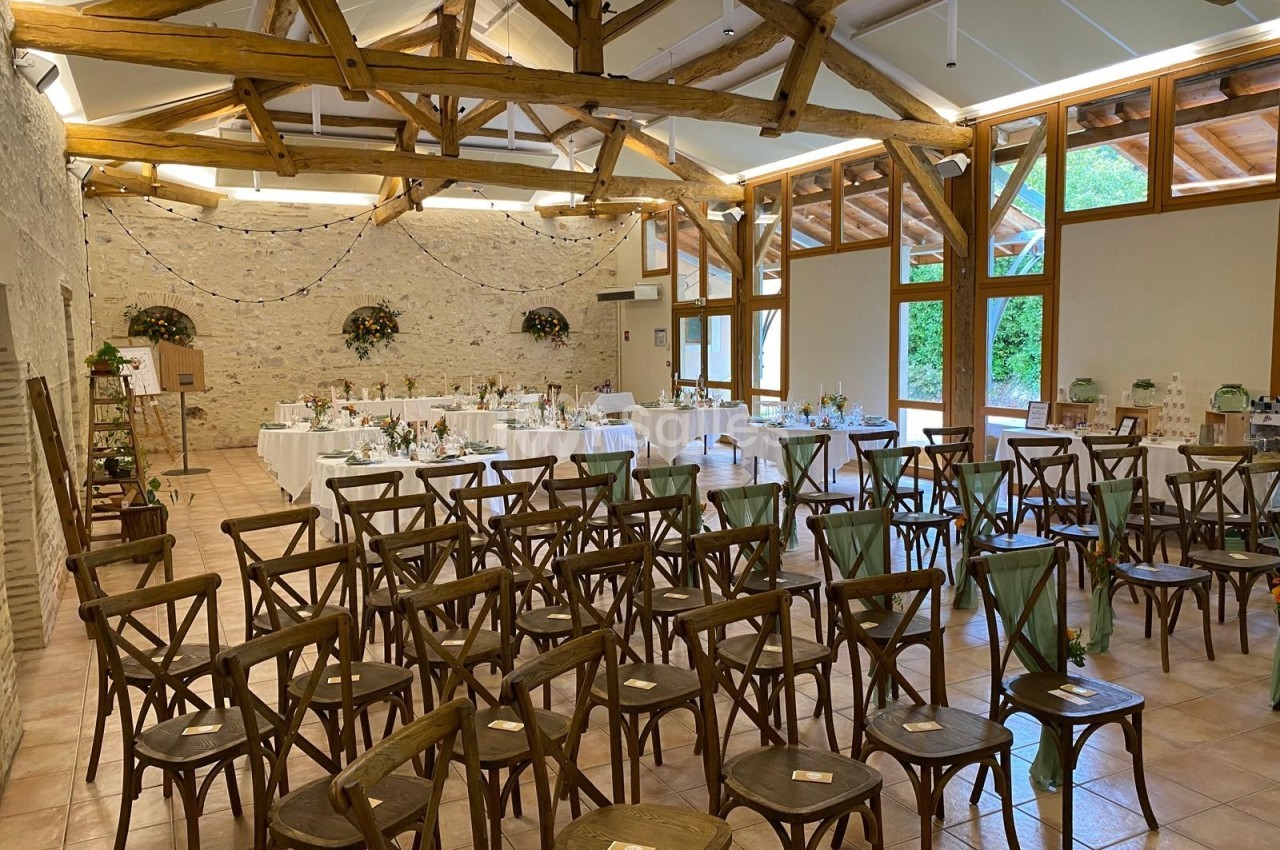 Salle de réception lumineuse avec des chaises en bois disposées face à des tables décorées pour un événement festif.