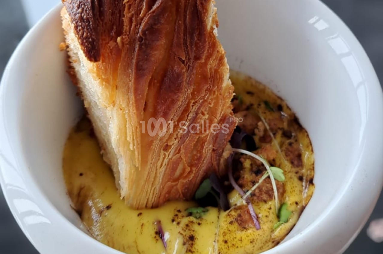 Feuilleté doré plongé dans une sauce crémeuse garnie de jeunes pousses dans un bol blanc.