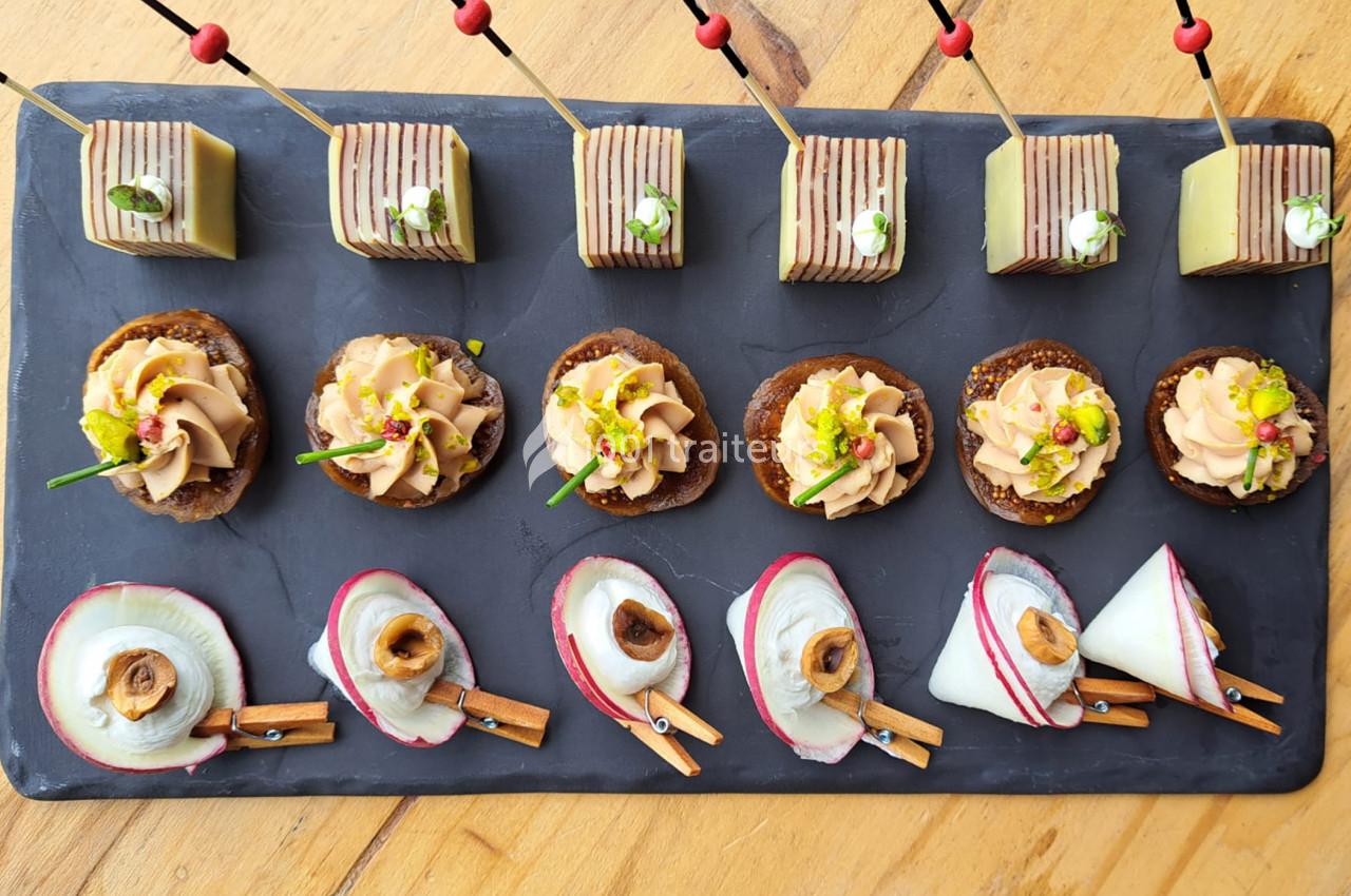 Plateau d'amuse-bouches variés disposés sur une ardoise, comprenant canapés, fromages et bouchées décorées.