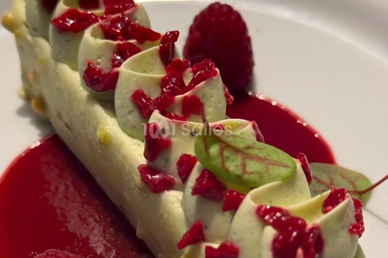 Dessert raffiné composé d'une mousse blanche garnie de morceaux de framboise, sur un coulis rouge, décoré d'une feuille…