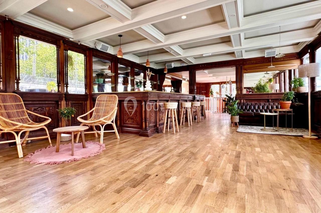 Intérieur lumineux avec parquet, mobilier en bois sculpté, fauteuils en rotin et plantes décoratives.