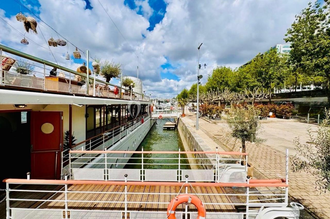 Bateau amarré le long d'un quai bordé d'arbres, sous un ciel partiellement nuageux.