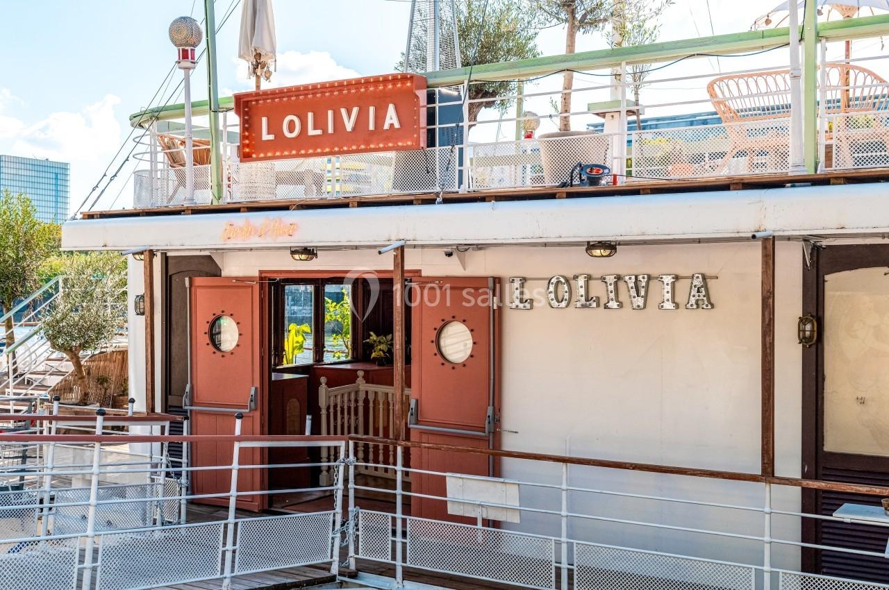 Façade d'un bateau aménagé avec des portes ouvertes, des chaises en terrasse et une enseigne ’L'OLIVIA’.
