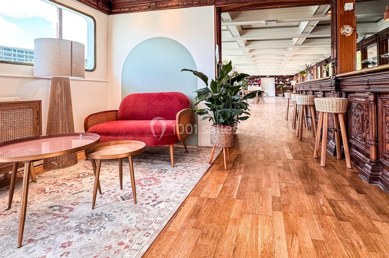 Salon lumineux avec canapé rouge, tables basses, plante verte et parquet, dans un espace au décor boisé et raffiné.