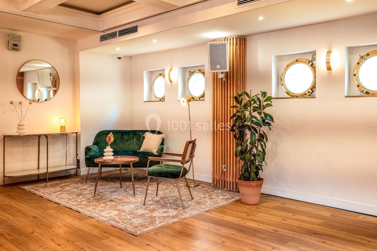 Salon lumineux avec canapé vert, table basse, plante en pot et hublots ronds sur un mur blanc.