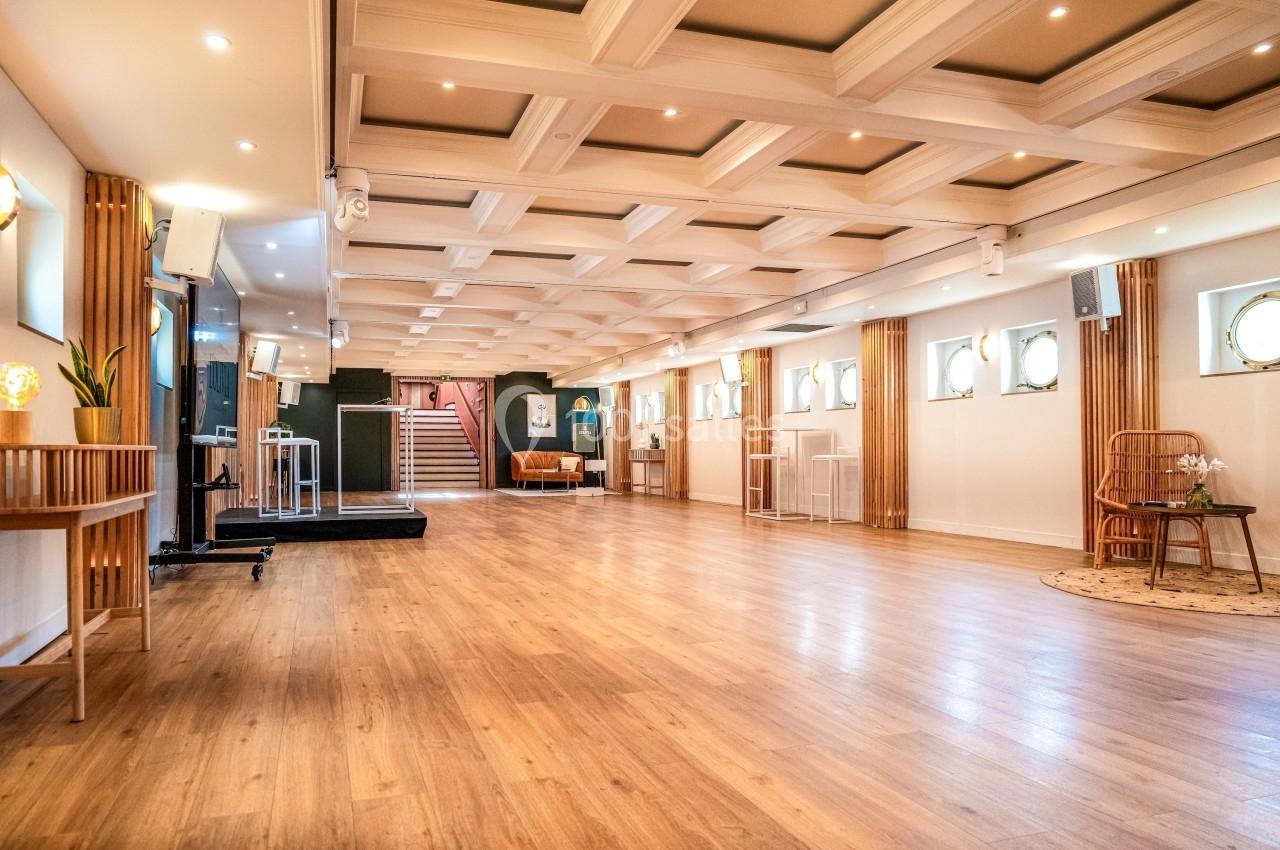 Salle lumineuse avec parquet, plafond à caissons, mobilier en bois et espace aménagé pour des événements.